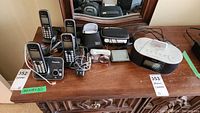 Overview of the lot showing Panasonic cordless phones on base, Sony Cyber-shot camera, Garmin navigation device, and home docking clock radio on a wooden surface.