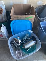 Top-down view of blue plastic bin containing two electric kettles, glass plates, and a pink glass bowl