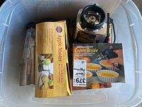 Plastic bin with cream brulee torch box, Osterizer blender jar with blade, Apple Master apple peeler box, and other items.