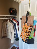 View of several women's jackets hanging on a rack, plus several reusable shopping bags hanging on a door hook