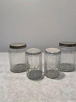 Photo showing four antique glass jars with metal lids in two distinct designs: ribbed side jars and octagonal side jars.