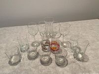 Thirteen assorted glasses arranged on a countertop, including wine glasses, festive glasses with Santa decals, and various smaller glasses.