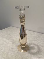 Photo of a single tall frosted glass candlestick with a clear glass candle holder at the top, displayed on a light surface against a neutral background