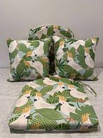 Photo showing three cushions with tropical bird and leaf pattern, two square cushions in front and a rectangular cushion with tie backs in back.