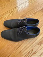 Top view photo of Rieker men's dress shoes size 10 showing the black textured upper, laces, and blue interior lining on a wood floor.