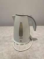 White Salton electric kettle on a gray surface with power cord coiled on detachable base.