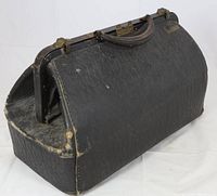 Photo displaying the front side of the antique pressed leather bag showing its worn black leather, metal frame with locks, leather handle, and visible signs of age.