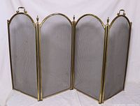 Four-panel brass fireplace screen shown fully extended, displaying the brass frame and mesh panels with handles on the outer panels.