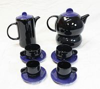 Overhead photo showing the entire coffee and tea set in blue and black ceramics including coffee pot, tea pot with warmer, two tea cups with saucers, and two demi-tasse cups with saucers.