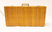 Closed rectangular rattan suitcase/trunk showing woven rattan exterior with handle on top.