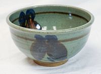 Side view of green ceramic bowl showing brown and blue brushstroke decoration on outside and footed base.
