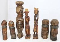 Full view of 8 wooden carved figures, mix of male and female heads and full figures varying in size from 9 to 17 inches tall, with distinct carving styles and natural wood patina.