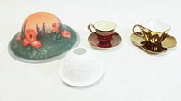 Photo showing the floral hand-painted glass lampshade, red teacup with saucer, gold metallic teacup with saucer, and white porcelain tea candle set arranged on a flat surface.