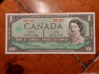 Front view of the 1867-1967 Canadian Centennial one dollar bill lying flat on a wooden surface.