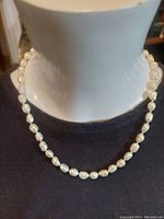 Front view of the original seed pearl necklace displayed on a mannequin bust wearing a dark top, showing small lustrous pearls and strand.