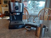 DeLonghi espresso and latte maker with accessories on countertop including frothing pitcher and portafilter.