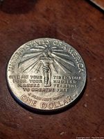Close-up of reverse side of coin depicting Liberty's torch with light rays and inscriptions United States of America, one dollar, and poem excerpt about tired, poor masses yearning to breathe free.