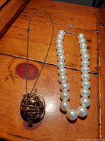 Both necklaces laid flat on a wooden surface showing pearl choker and gyroscope pendant chain.