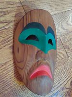 Front angled view of handcrafted North West First Nations cedar carved mask showing carved wood grain with green painted eye area and red lips.