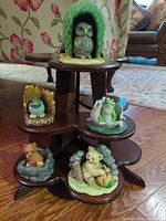 Original three-tiered dark wooden display stand with several porcelain woodland animal figurines arranged on it including an owl, bluebird, frog, fox, and bear.