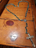 Full view of the vintage Catholic rosary showing blue glass beads and metal crucifix laid out on a wooden surface.