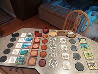 Photo showing full array of coasters arranged on countertop, including wooden, ceramic, metal, and painted coasters along with wooden bowl and coaster holders.