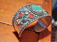 Side angled view showing the layered silver bead and twisted wire detailing around the large green oval stone and smaller surrounding stones inset in silver cuff bracelet.