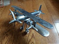 Side view of the vintage handcrafted aluminum biplane showing dual engines with propellers, top wing, and floating landing gear.