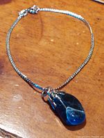 Silver bracelet laid flat showing the polished blue stone pendant and sterling silver chain.