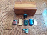 Photo of the Lane cedar hope chest salesman sample and seven vintage lighters of various styles and materials on a wood floor.