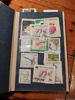 Blue vintage album with stamps mounted on black stock pages, showing diverse themes including Polish flora, fauna, and cultural designs.