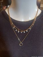 The necklace displayed on a mannequin showing the three strands with bead and disc charms and a circular pendant on the lowest strand.