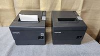 Top front view of two Epson TM88-V receipt printers showing the paper feed slot and front branding. One has paper inserted.