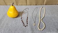 Lot of 3 necklaces with a yellow pear for scale, showing relative sizes and details of each necklace
