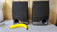 Pair of Pioneer bookshelf speakers with fabric grills on, showing front side and port holes alongside a banana for scale.