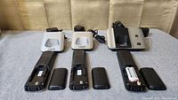 Set of three VTech cordless phone handsets arranged in front of two white charging bases and one black and silver base station. Two handsets have battery compartments open and show one with battery installed.