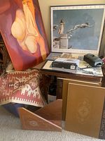 Photo showing framed abstract painting, framed Michael Parkes print, Navajo style wall rug, boxed Polaroid frame, Arab Islamic art books, and wooden holder arranged together.