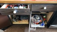 Open cabinet and drawer showing variety of baking pans, mixing bowls, strainers, and other baking tools.