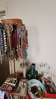 Photo shows multiple colorful beaded necklaces hanging on a standing rack along with various rings and bracelets displayed below.