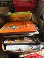 Top view of a box filled with assorted books, including visible titles like a bright orange book titled 'The North American Indian' and a Michael Harding book.
