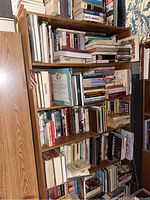 Wooden bookshelf filled with assorted books, some horizontally stacked, various genres visible.