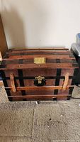 Front view of wooden trunk showing dome-top, black metal bands, leather straps and brass latch