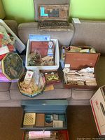 Wide view showing several handcrafted wooden boxes filled with assorted buttons, some labeled, along with sewing kits and vintage tools placed on a couch.