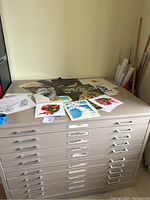 Two beige metal flat file cabinets stacked, closed drawers, prints on top