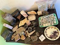 Main set of mineral specimens displayed on black table including petrified wood, Alaska jade, geodes, boxed mineral specimens, and packed minerals.