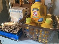 Photo showing six full gallon bottles of Arm & Hammer laundry detergent with a box of wooden clothes pins and a boxed Crane Ultrasonic Cool Mist Humidifier in background