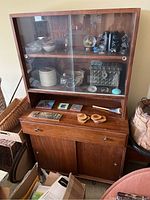 Full frontal view of two-piece mid-century modern hutch with glass display doors on top and wooden drawer and doors below, showing general condition and contents removed.