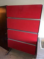 Closed view of a metal office cabinet with four red front panels and black sides on metal legs.
