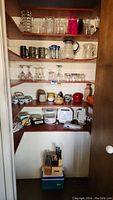 Full pantry shelves showing a wide variety of glassware, mugs, pitchers, ceramic containers, and small kitchen appliances below.