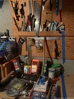 Wide view of assorted tools including hand saws, brushes, clamps, utility knives, and small containers of hardware.